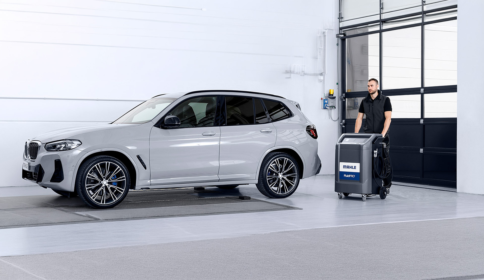 Techniker rollt das MAHLE-Getriebespülgerät zu einem Fahrzeug in der Werkstatt